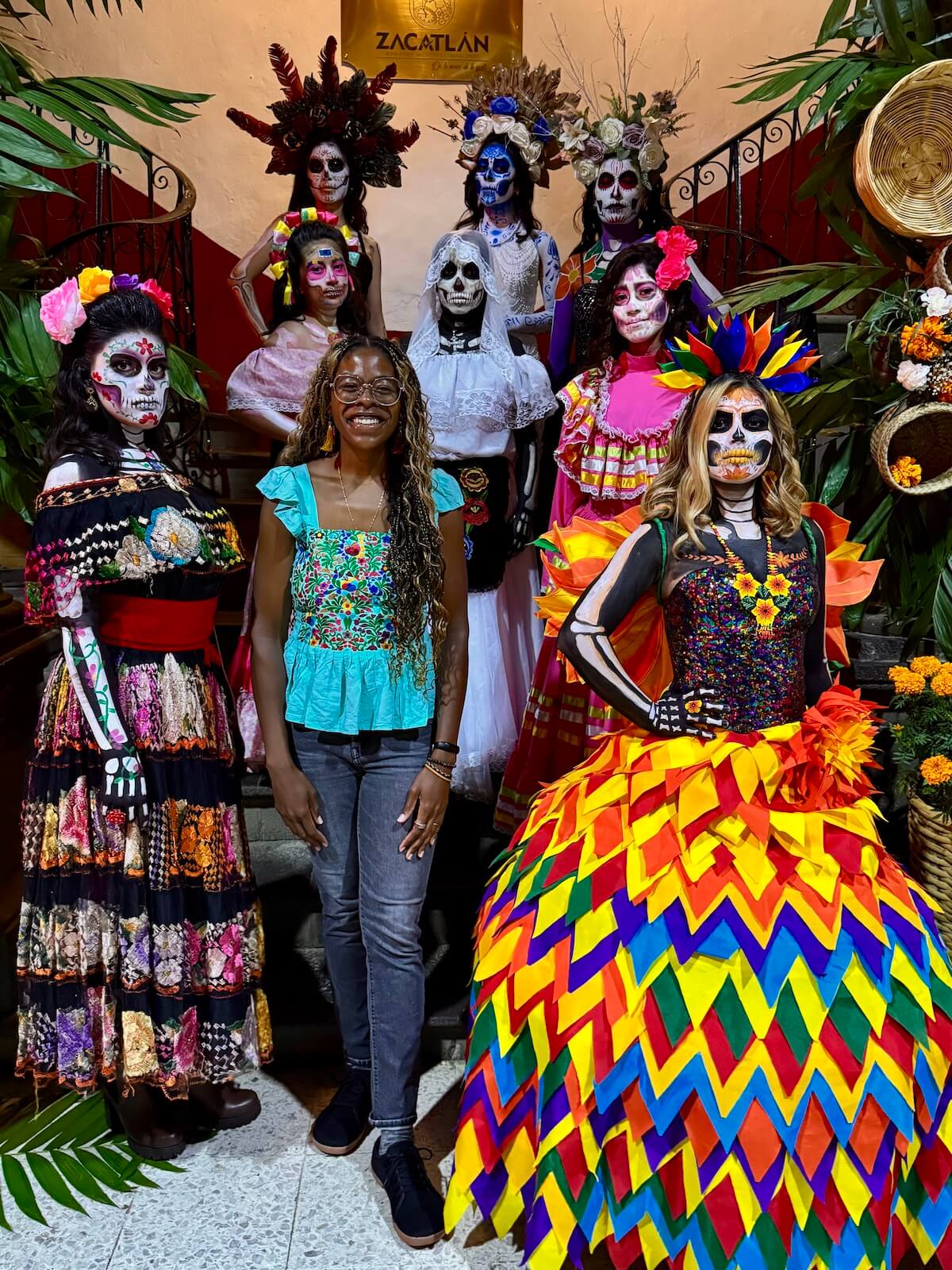 A photo of me smiling with women dressed in elegant gowns, skull-painted faces, and flower crowns.