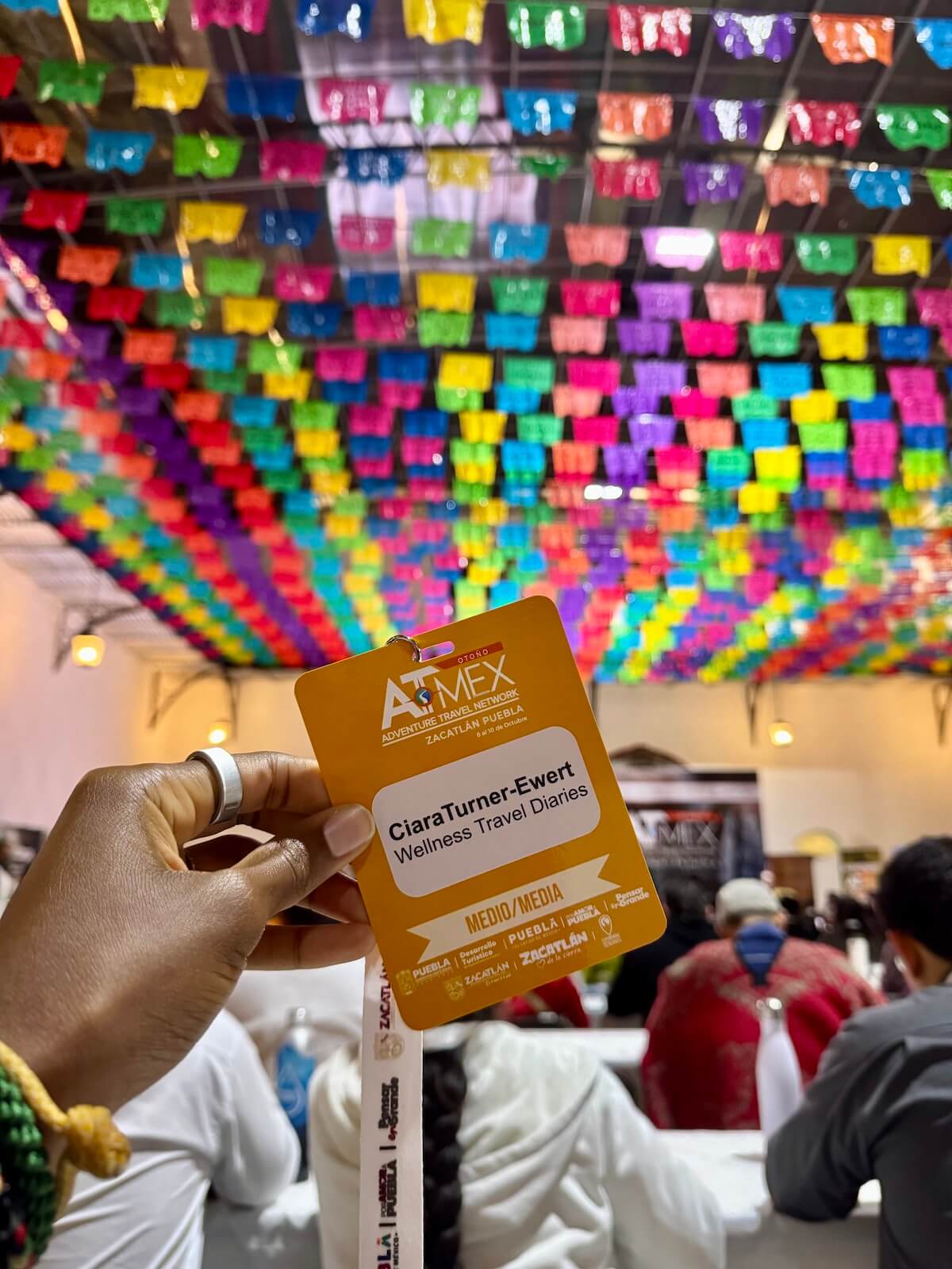 Holding my official media badge beneath colorful flags at the ATMEX conference.