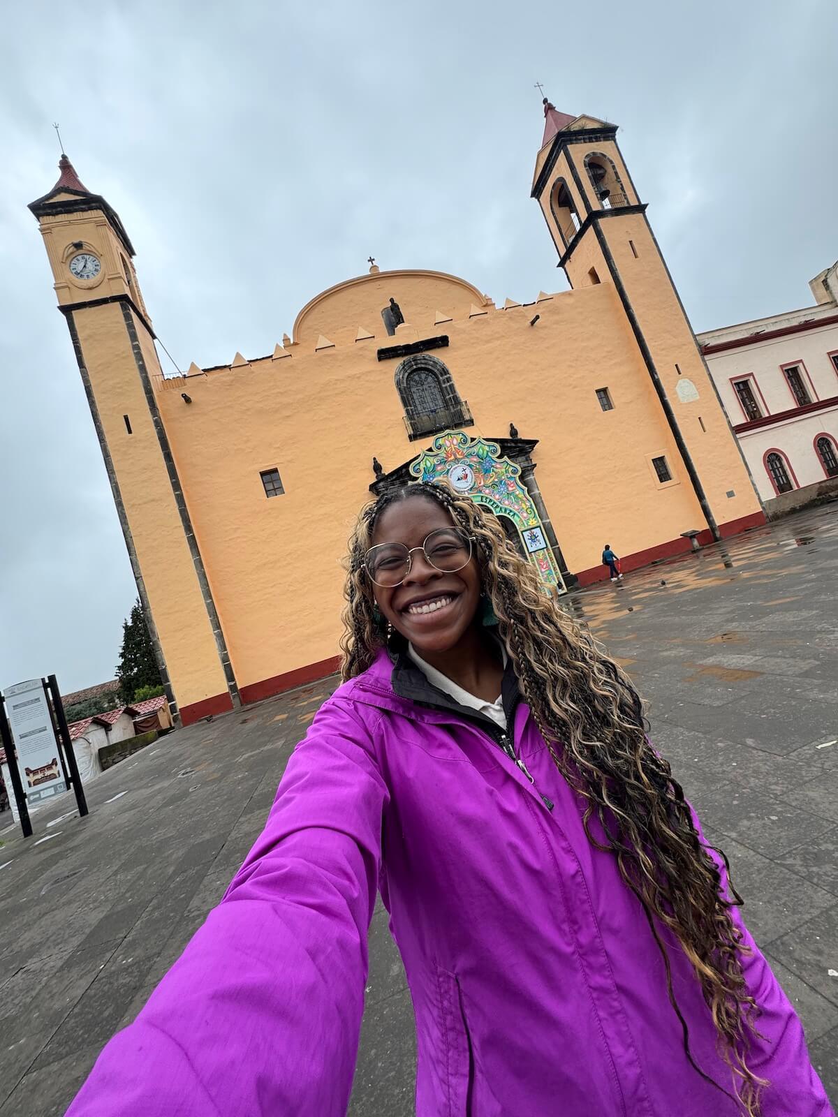 Me smiling in front of a yellow church in Zacatlan, Mexico.