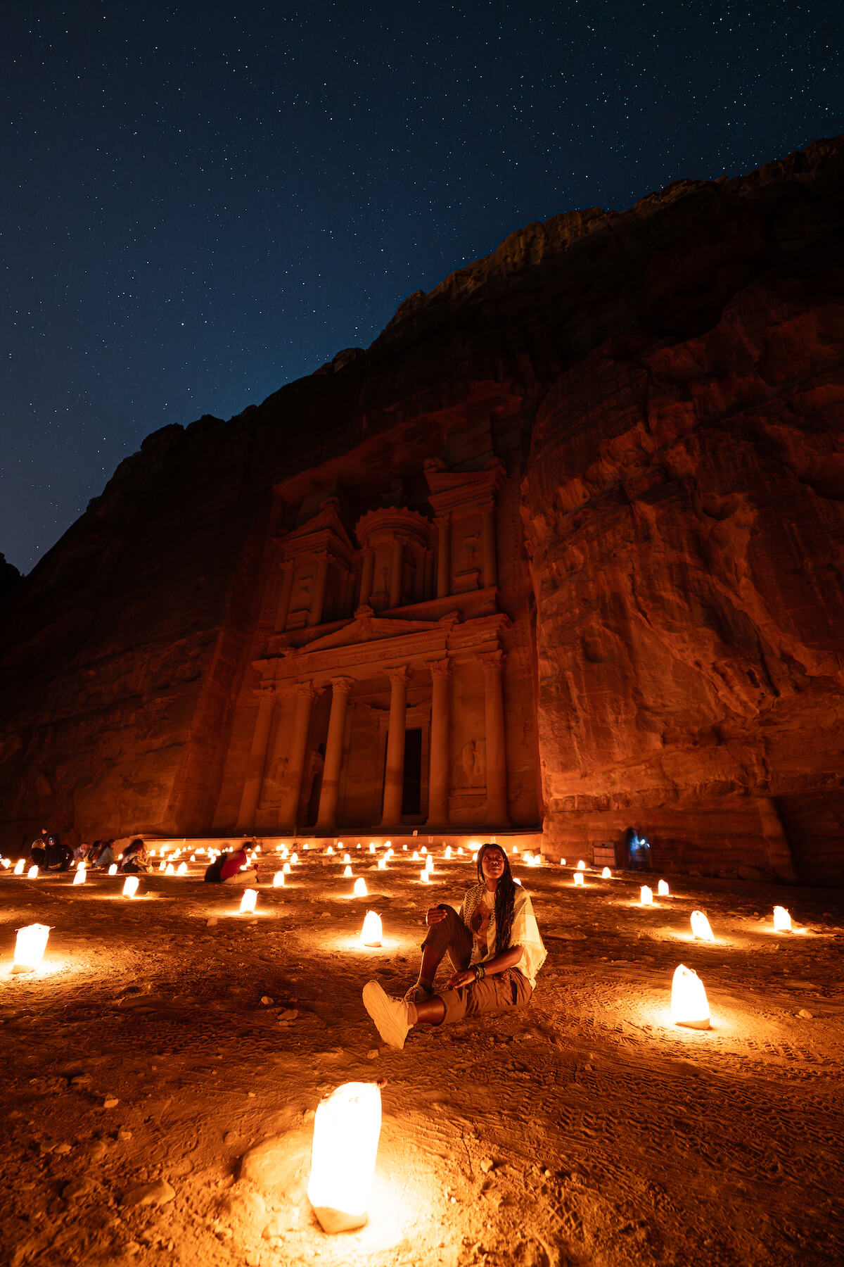 A picture of Petra sitting in front of Petra at night on the dirt in front of the monastery.